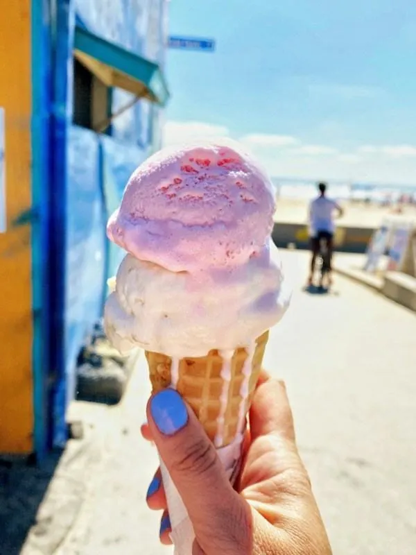 Une main tient une glace rose et blanche sur une plage