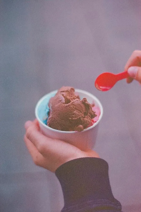 Une main tient un pot de glace au chocolat avec une cuillère rouge