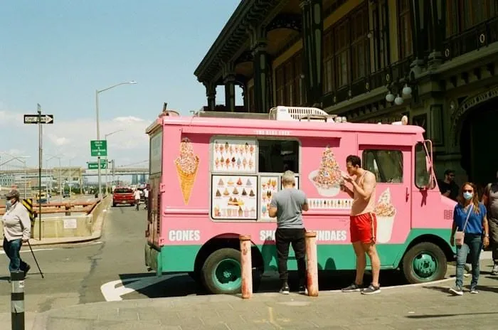 Un camion de glaces rose devant une rue animée